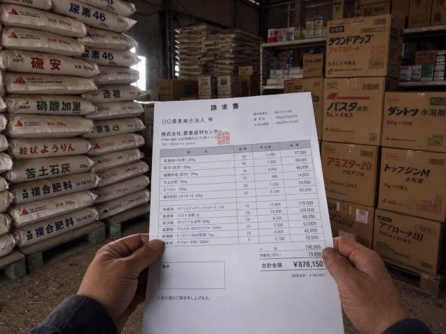 倉庫に積み上げられた大量の肥料袋と高額な請求書を持つ手