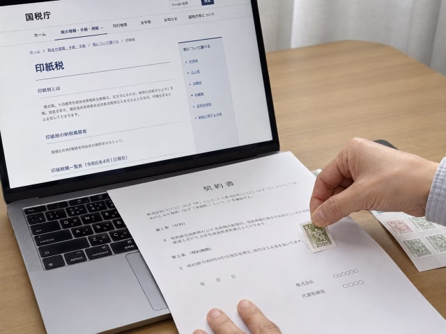 パソコンで調べながら契約書に収入印紙を貼る様子