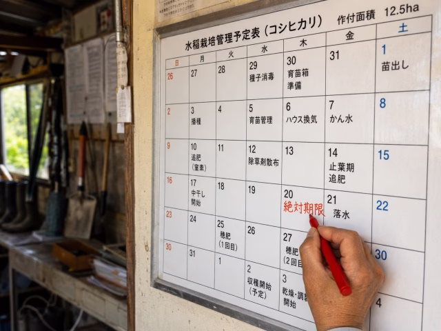 大きなカレンダーの「防除適期(4月10日)」に、太い赤ペンで「絶対期限」と書き込んでいる日本の農家の手元。