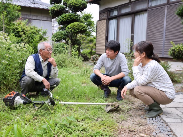 実家の庭を前に草刈機を買うかレンタルにするか相談する親子